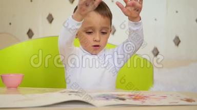 一个淘气的男孩拿颜料在纸上拍掌。孩子的发展、教育、心理、情感。